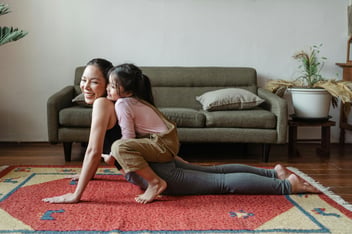 middle age mom performing a static stretch while daughter sits on her back